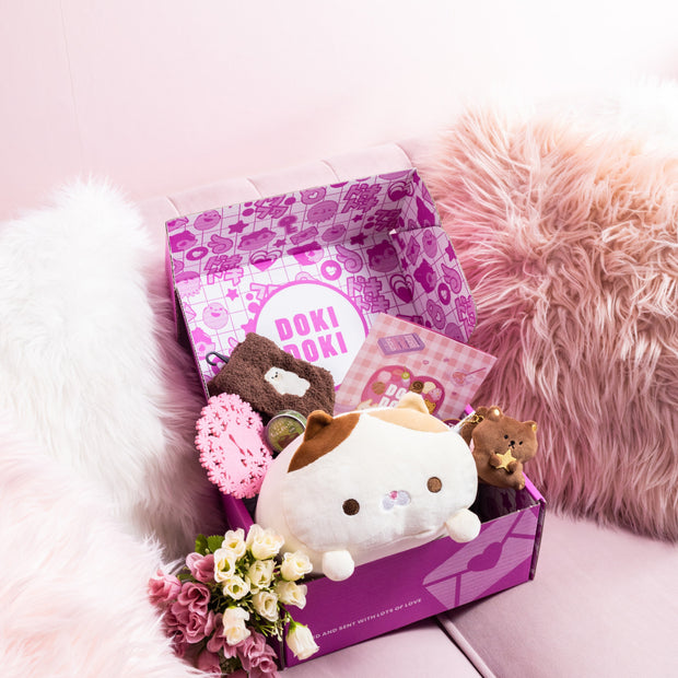 A Doki Doki Kawaii Crate by Japan Crate, filled with kawaii Japanese plushies, flowers, and stationery, sits on a light pink sofa with fluffy pillows.