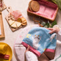 During a picnic setup with snacks and a cozy blanket, someone holds the Doki Doki Kawaii Crate towel from Japan Crate, featuring blue fabric and adorable white cat designs—ideal for fans of Sanrio or Japanese plushies. thumbnail 3